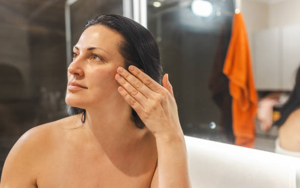 Woman examining her face in mirror in bathroom.