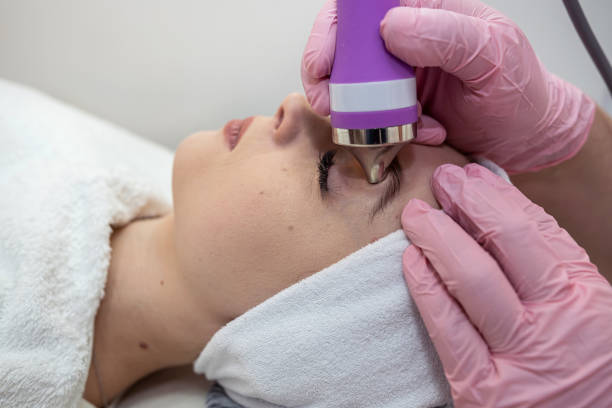 A woman receiving a facial treatment with a professional using a modern skin care device.