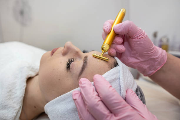 A woman receiving a facial treatment with a gold roller tool in a spa setting.