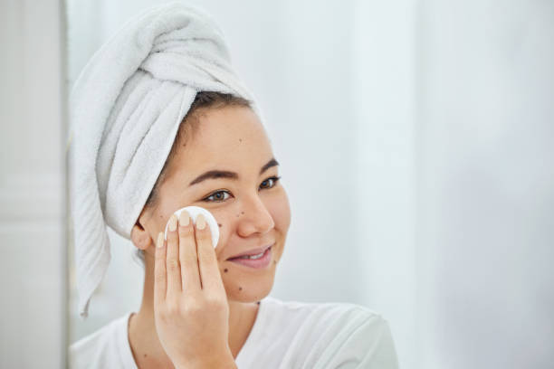 Smiling woman applying facial skincare product with towel on her head